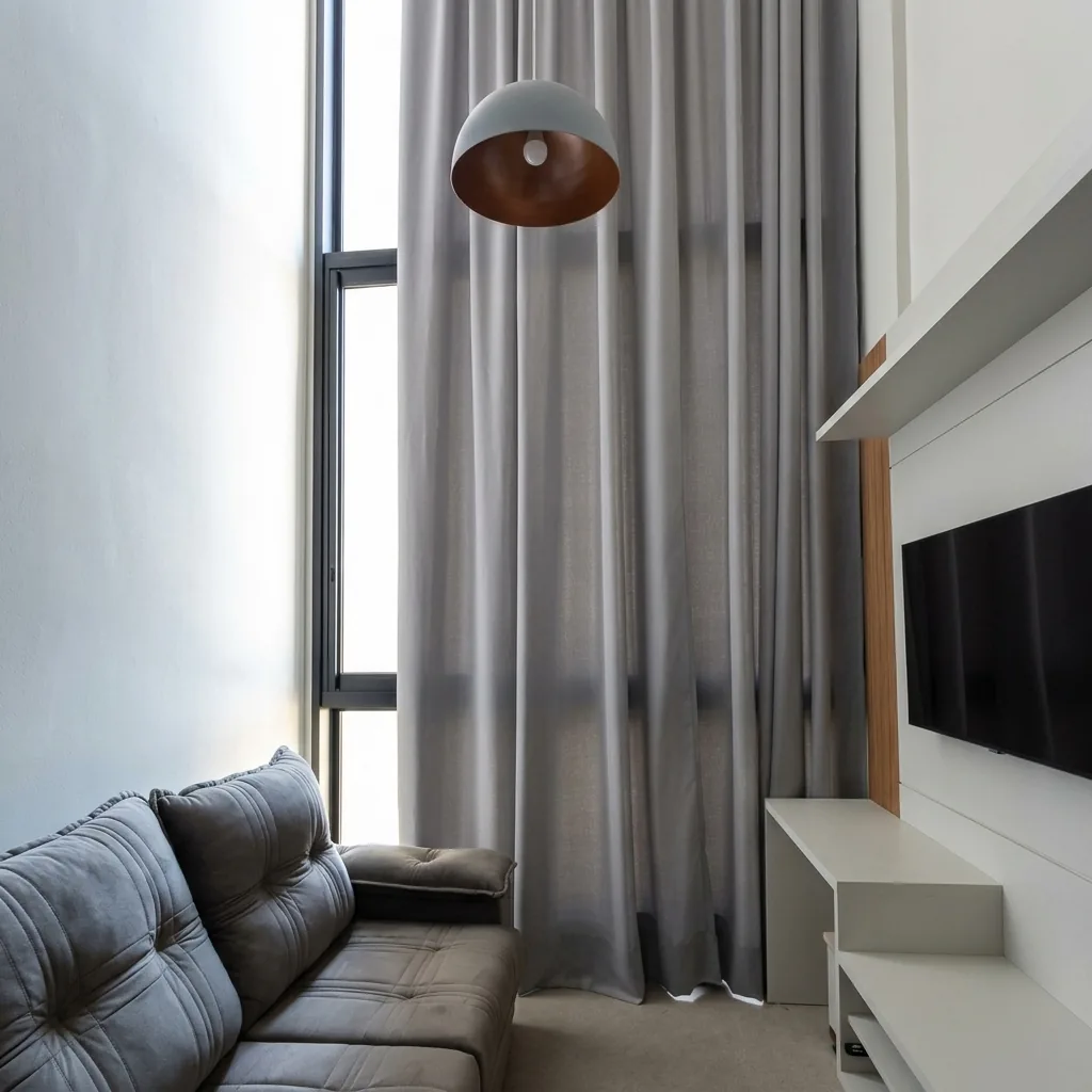 Cortinas de tecido do teto ao chão em sala de pé-direito duplo com luminária pendente — projeto Entre Tramas em Piracicaba